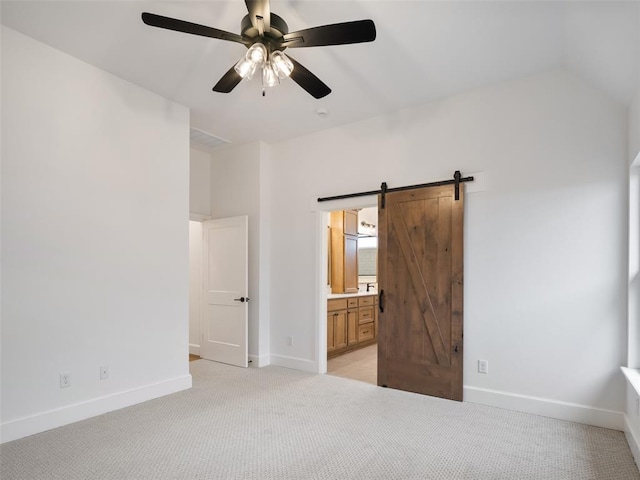 unfurnished bedroom with light carpet, vaulted ceiling, baseboards, and a barn door