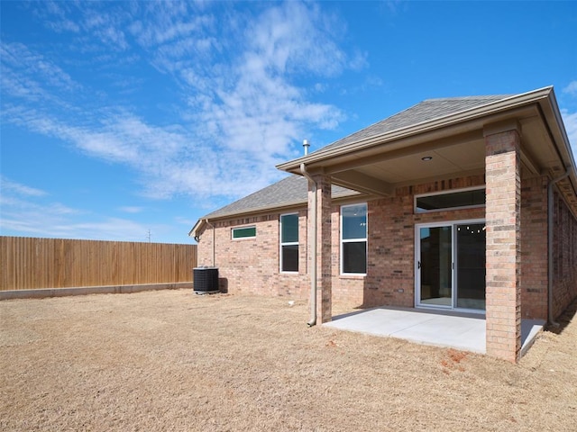 rear view of house featuring a shingled roof, fence, cooling unit, a patio area, and brick siding