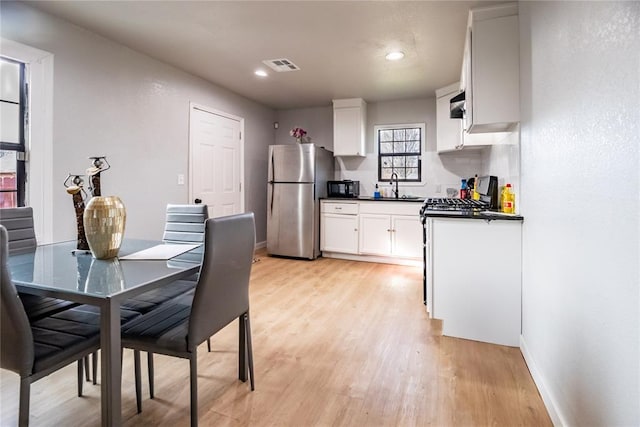 kitchen with light hardwood / wood-style flooring, sink, stove, white cabinets, and stainless steel refrigerator