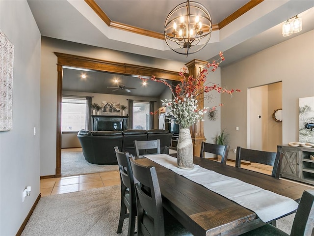 carpeted dining space with crown molding, a tray ceiling, and ceiling fan with notable chandelier