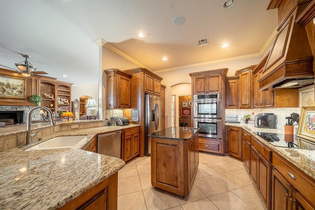 kitchen with sink, appliances with stainless steel finishes, light stone counters, custom exhaust hood, and kitchen peninsula