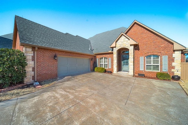 view of front of property featuring a garage, stone siding, brick siding, and roof with shingles