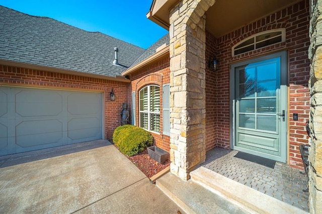 entrance to property with driveway, a shingled roof, an attached garage, and brick siding