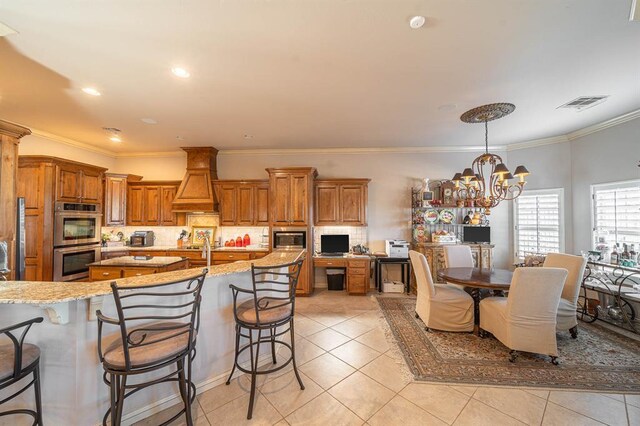 kitchen featuring visible vents, brown cabinetry, decorative backsplash, appliances with stainless steel finishes, and premium range hood