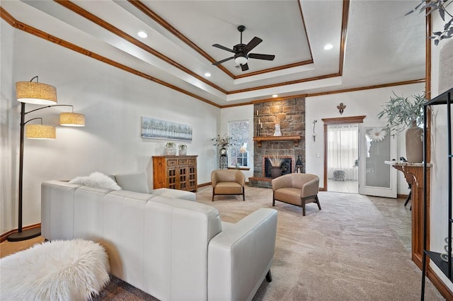 carpeted living room featuring ornamental molding, a large fireplace, ceiling fan, and a tray ceiling