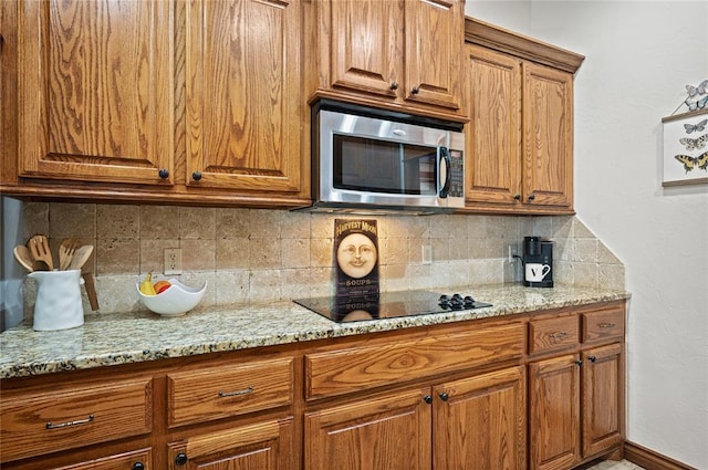 kitchen featuring black electric cooktop, tasteful backsplash, and light stone counters