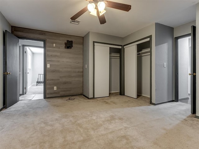 unfurnished bedroom featuring ceiling fan, wooden walls, and light carpet