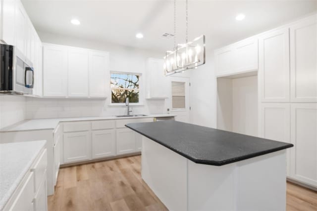 kitchen featuring sink, white cabinetry, a center island, decorative light fixtures, and light wood-type flooring