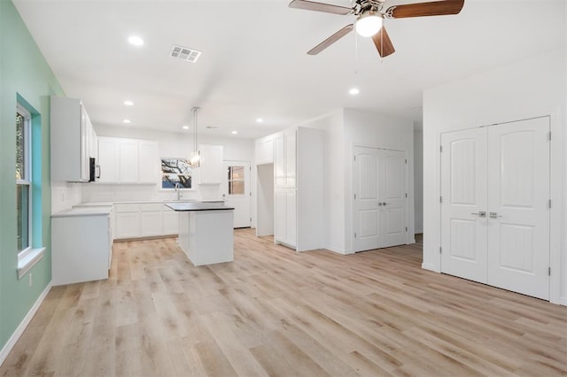 kitchen featuring decorative light fixtures, light hardwood / wood-style floors, a kitchen island, and white cabinets