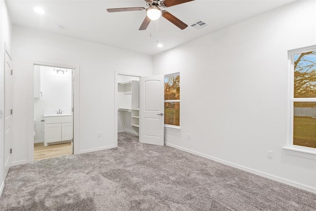 unfurnished bedroom with connected bathroom, a walk in closet, ceiling fan, light carpet, and a closet