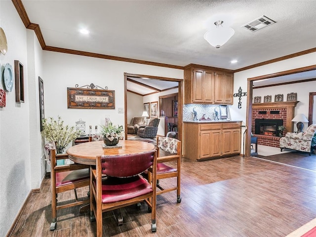 dining room with hardwood / wood-style floors, ornamental molding, and a brick fireplace