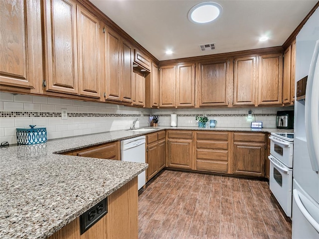 kitchen with sink, tasteful backsplash, white appliances, light stone countertops, and hardwood / wood-style floors