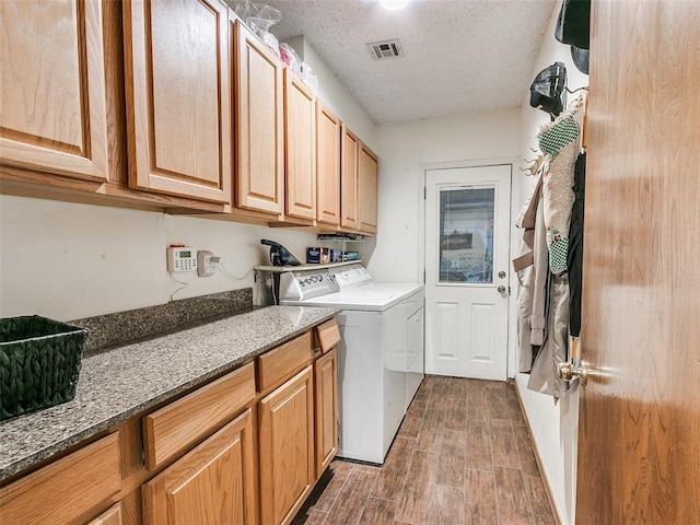 clothes washing area with cabinets, a textured ceiling, and washer and clothes dryer