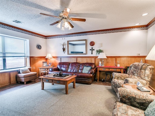 living room featuring ceiling fan, crown molding, a textured ceiling, and wood walls