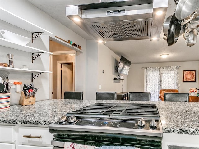 kitchen with extractor fan, light stone countertops, gas stove, and white cabinets