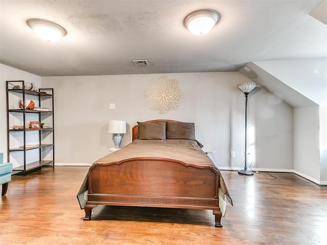 bedroom featuring lofted ceiling, wood-type flooring, and a textured ceiling