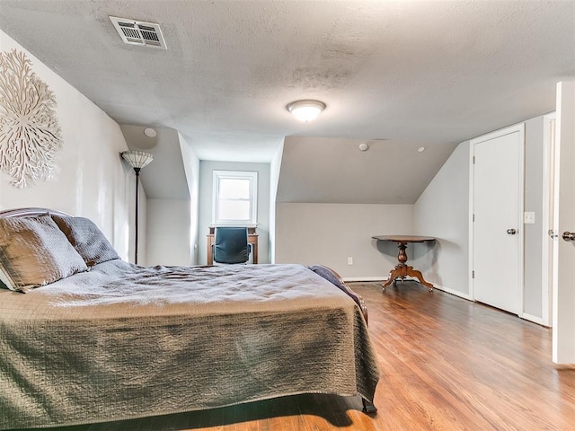 bedroom featuring hardwood / wood-style flooring, lofted ceiling, and a textured ceiling