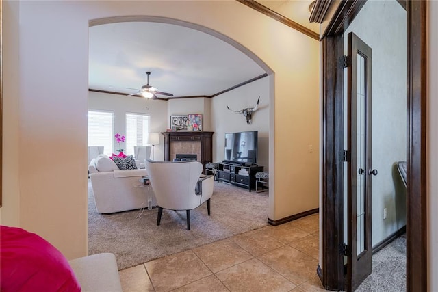 tiled living room with crown molding, ceiling fan, and a tile fireplace