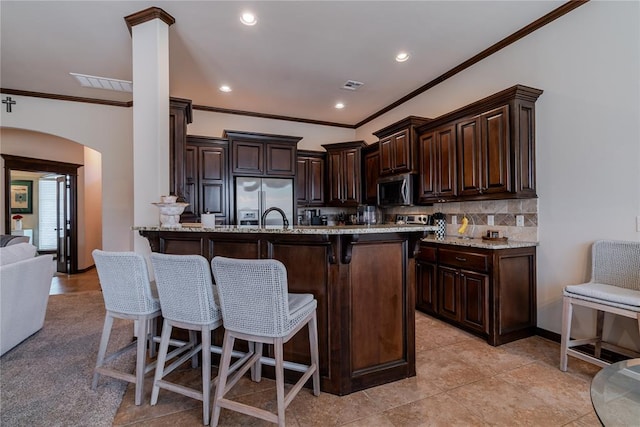 kitchen featuring dark brown cabinetry, a kitchen bar, stainless steel appliances, light stone countertops, and backsplash