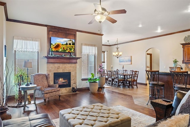 living room featuring a tile fireplace, ornamental molding, ceiling fan with notable chandelier, and light wood-type flooring