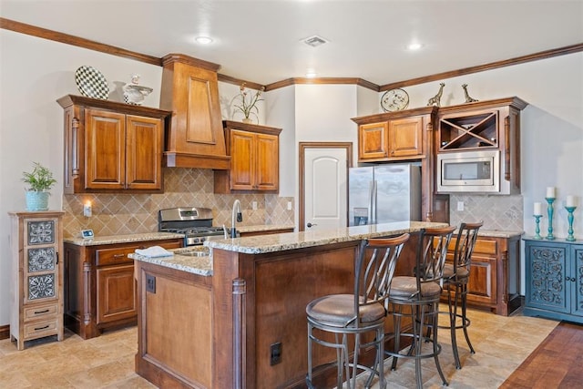 kitchen with stainless steel appliances, premium range hood, light stone countertops, and a center island with sink