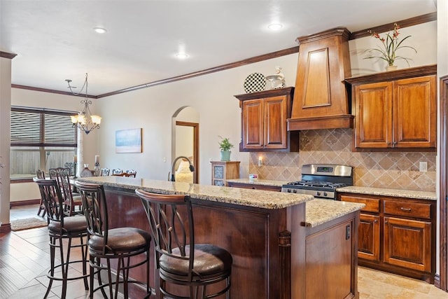 kitchen with stainless steel range oven, light stone counters, custom range hood, pendant lighting, and a kitchen island with sink