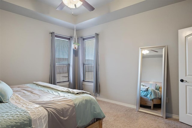 carpeted bedroom with ceiling fan and a tray ceiling