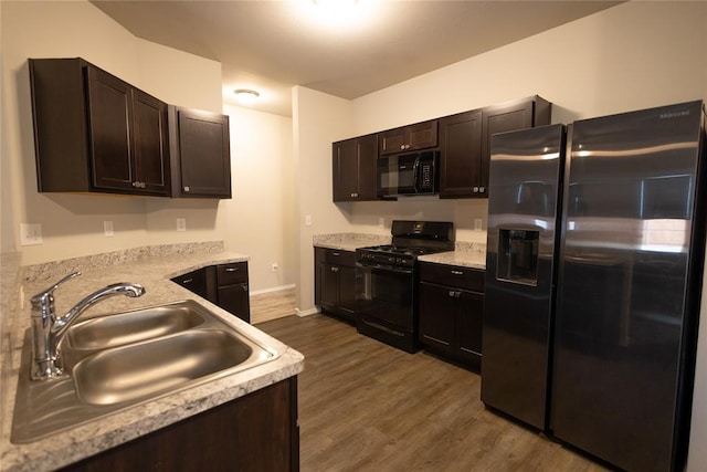 kitchen featuring black appliances, sink, light stone counters, dark brown cabinetry, and dark wood-type flooring