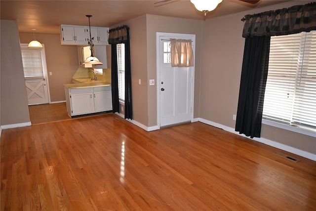 interior space with sink, decorative light fixtures, light hardwood / wood-style flooring, ceiling fan, and white cabinets