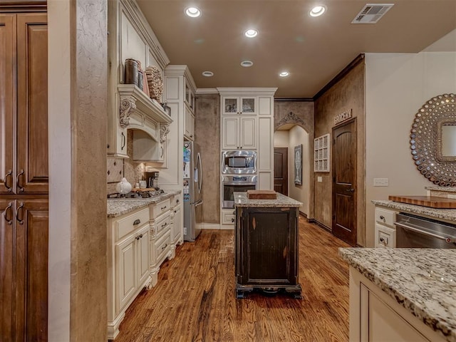 kitchen with stainless steel appliances, dark hardwood / wood-style flooring, ornamental molding, and light stone counters