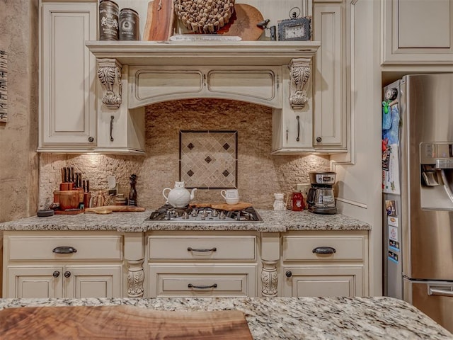 kitchen with backsplash, cream cabinets, light stone countertops, and appliances with stainless steel finishes