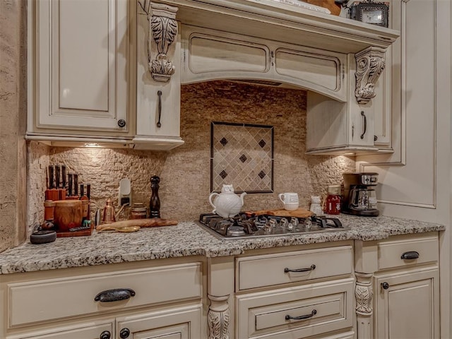 kitchen featuring stainless steel gas stovetop, light stone countertops, backsplash, and cream cabinets