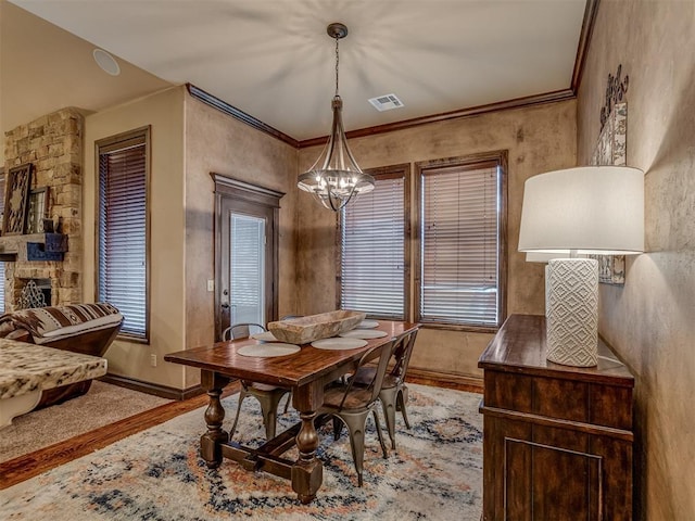 dining space with light hardwood / wood-style flooring, a notable chandelier, crown molding, and a stone fireplace