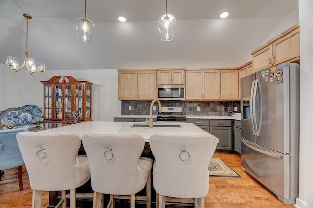 kitchen with pendant lighting, appliances with stainless steel finishes, sink, and a kitchen island with sink