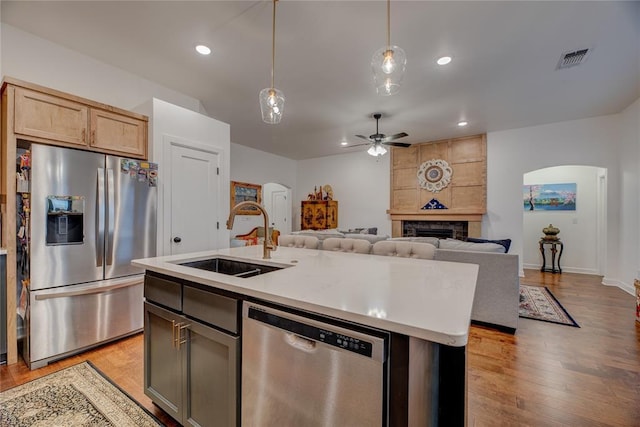 kitchen featuring appliances with stainless steel finishes, pendant lighting, sink, light brown cabinets, and a center island with sink