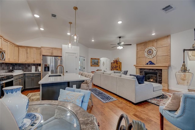 kitchen with gray cabinets, an island with sink, hanging light fixtures, stainless steel appliances, and light brown cabinets