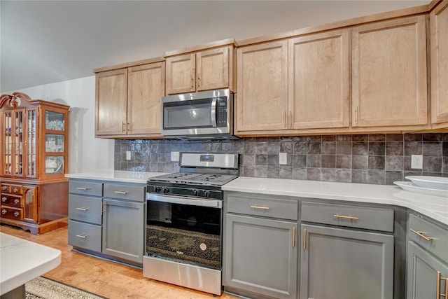 kitchen featuring tasteful backsplash, appliances with stainless steel finishes, gray cabinetry, and light wood-type flooring