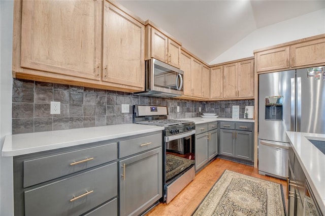 kitchen with lofted ceiling, light brown cabinetry, appliances with stainless steel finishes, gray cabinets, and decorative backsplash