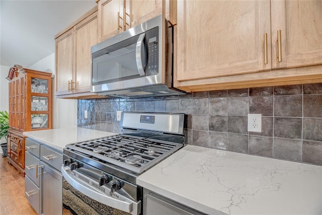 kitchen featuring light brown cabinetry, light stone counters, tasteful backsplash, and appliances with stainless steel finishes