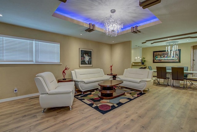 living room with a notable chandelier, a tray ceiling, and light wood-type flooring