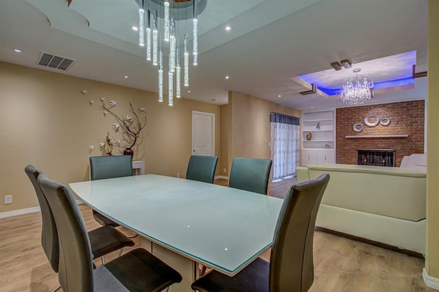 dining space featuring a fireplace, a notable chandelier, light hardwood / wood-style floors, and built in shelves