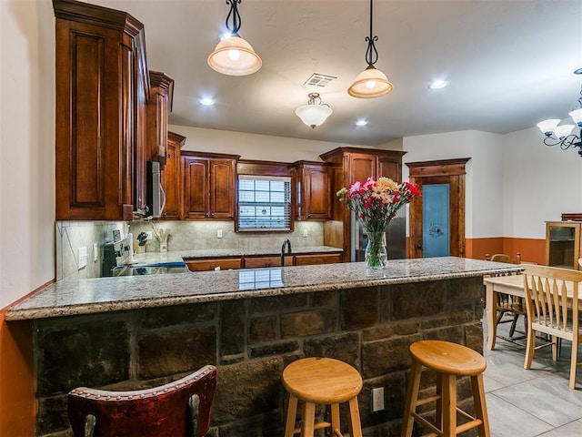 kitchen with a breakfast bar, stove, hanging light fixtures, backsplash, and kitchen peninsula