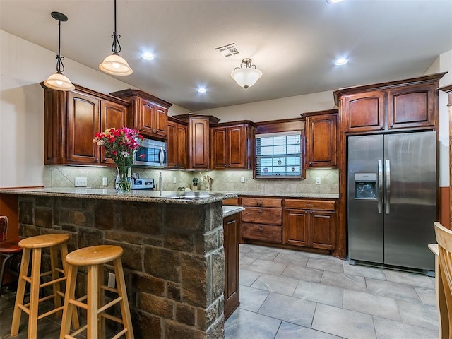 kitchen with appliances with stainless steel finishes, a breakfast bar, decorative backsplash, and dark stone counters