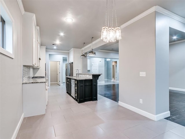 kitchen with an island with sink, ornamental molding, white cabinets, and decorative light fixtures