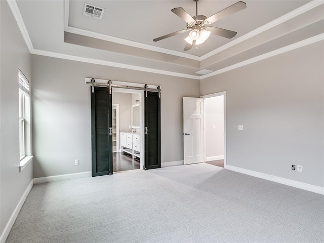 unfurnished bedroom with carpet floors, ornamental molding, a raised ceiling, and a barn door