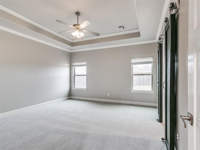 carpeted empty room with crown molding, ceiling fan, a tray ceiling, and a barn door