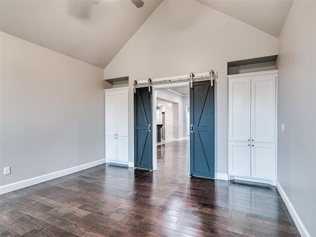 unfurnished bedroom featuring dark hardwood / wood-style floors, a barn door, and high vaulted ceiling