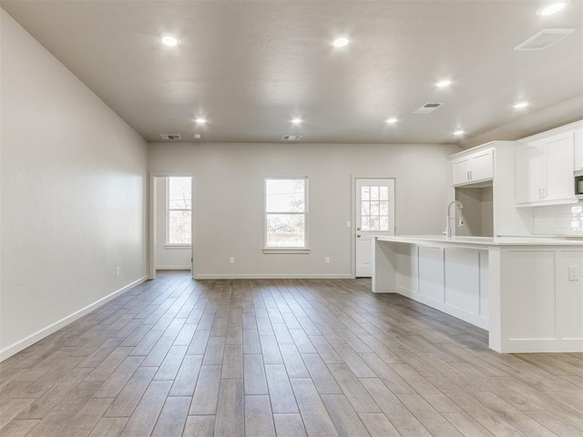 kitchen featuring white cabinetry, a kitchen bar, backsplash, and light hardwood / wood-style floors