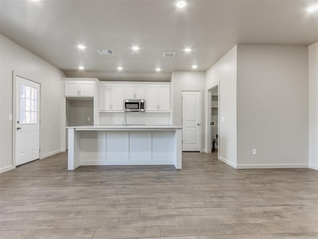 kitchen featuring tasteful backsplash, an island with sink, white cabinets, and light hardwood / wood-style flooring