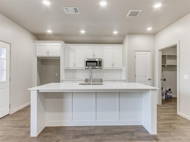 kitchen with tasteful backsplash, an island with sink, sink, and white cabinets